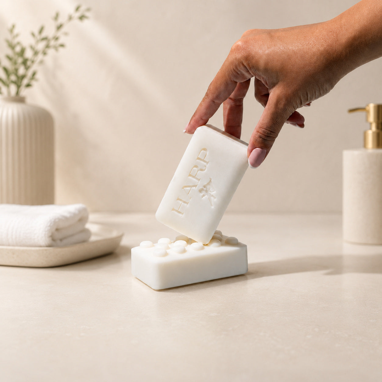 Hand holding a HARP body wash bar above a textured HARP bar