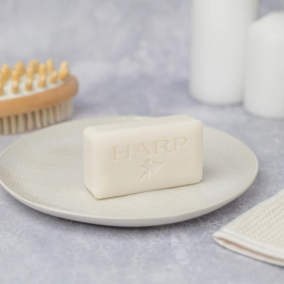 HARP cleansing bar resting on a draining dish beside a bath brush